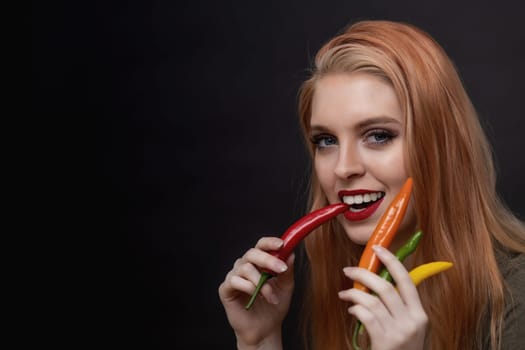 Attractive young woman with red lips is tasting red  chili pepper