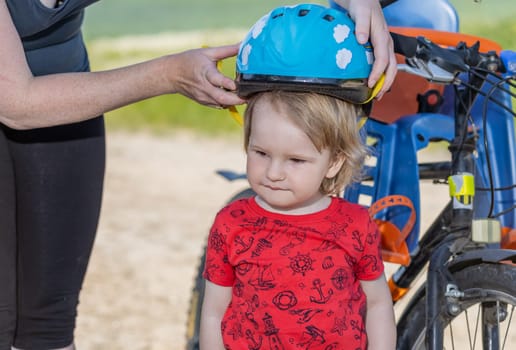 Mother puts on the  head of her little son safety bicycle helmet