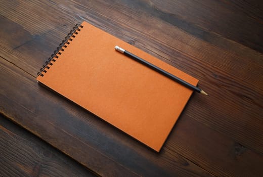 Orange notepad and pencil on wooden background. Blank stationery template.
