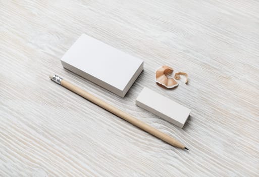Blank business card, pencil and eraser on light wooden background. Mock-up for branding identity.