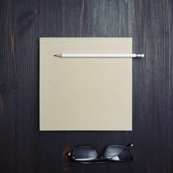 Photo of blank closed brochure, pencil and glasses on wooden background. Responsive design mockup. Stationery elements. Template for placing your design. Top view. Flat lay.