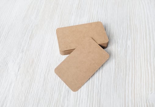 Photo of blank kraft business cards on light wood table background. Template for branding identity.