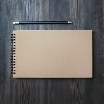 Blank kraft sketchbook and pencil on wooden background. Blank stationery mockup. Template for placing your design. Top view. Flat lay.