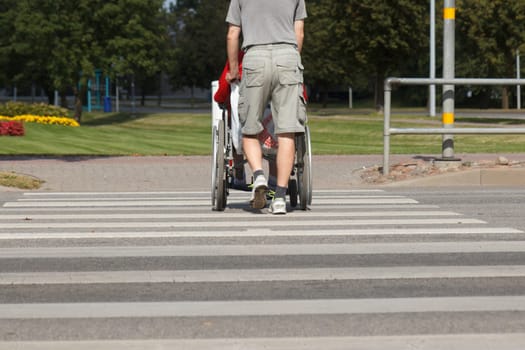 A man pushes wheelchair with disabled through pedestrian crossing
