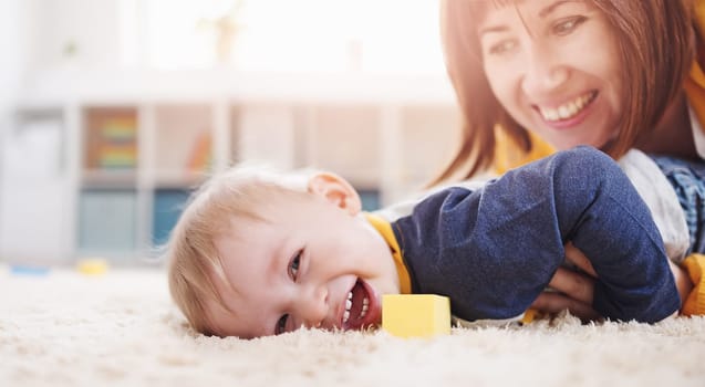 Mother playing with her cute son on the floor. Concept of the family relationship and mother's love.