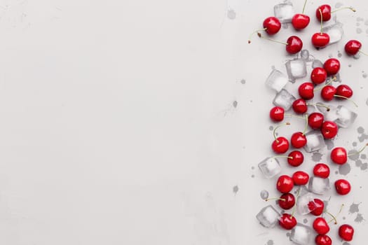 Flat lay top view on gray concrete background with sweet cherry berries and ice cubes. Freshness, summer conceptual minimal background. Eco, bio farm food and fruits concept with copy space area