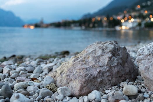 Rock in the foreground, cute little Italian village with lights in the background. Evening.