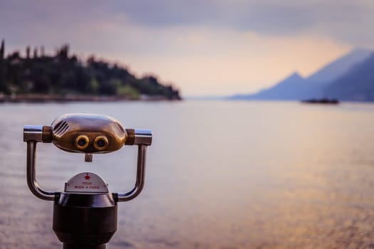 Tourist binoculars on the lake Lago di Garda, evening scene with water and mountains