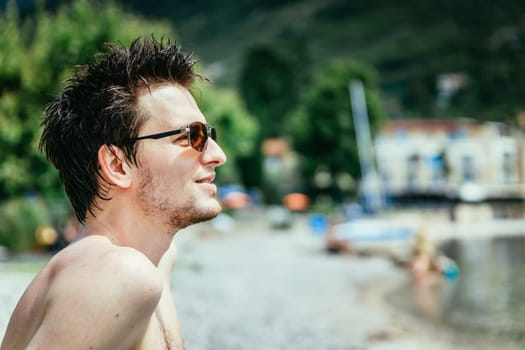 Young man with sunglasses is sitting on the beach and thinking