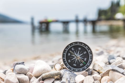 Close up of a nautical compass on the beach, coastline in the blurry background