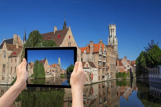 In the bottom left of the photo are hands holding tablet, whose screen contains color photo of the Rozenhoedkaail. Background of the photo contains the same color photo of the Old Town of Bruges (Bruges, Belgium)