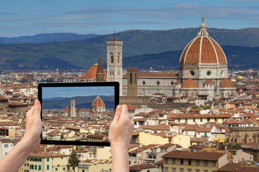 In the bottom left of the photo are hands holding tablet, whose screen contains color photo of the Cathedral Santa Maria del Fiore in Florencel. Background of the photo contains the same photo of the historic center of Florence (Tuscany, Italy)