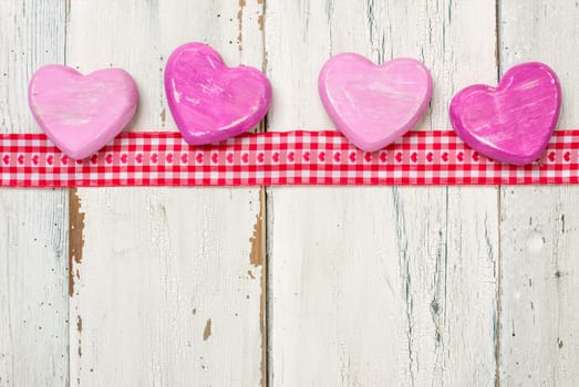 Gift ribbon with pink wooden hearts in front of white wooden boards