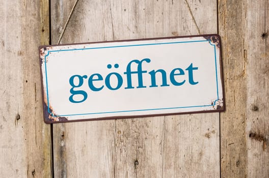 Old tin sign in front of rustic wooden wall - open