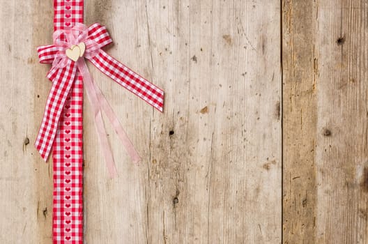 Red gift ribbons with bow in front of rustic wooden boards