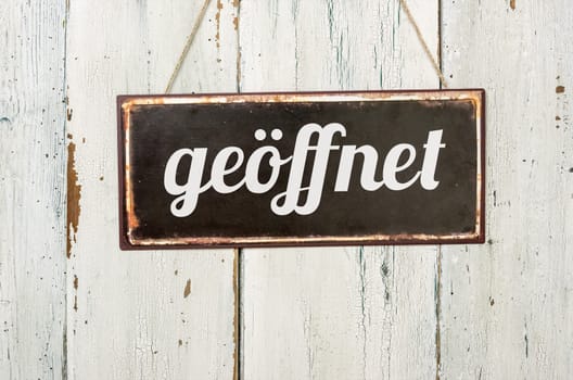 Old tin sign in front of white wooden wall - open