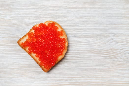 Sandwich with red caviar on light wood table background. Top view. Flat lay.