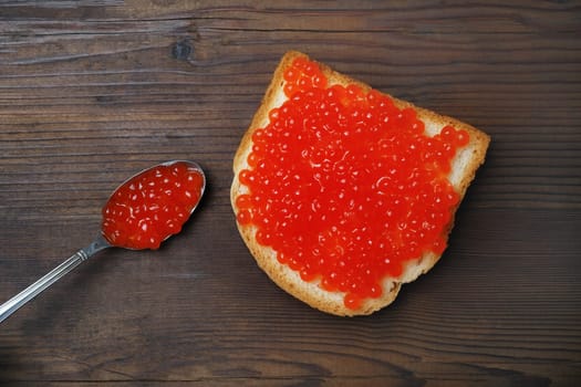 Sandwich with red caviar and spoon on wooden background. Flat lay.