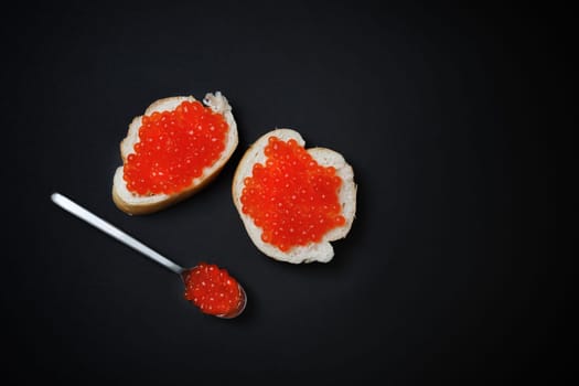 Sandwiches with red caviar and spoon on black background. Top view. Flat lay.