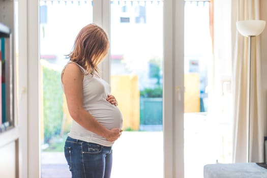 Happy Caucasian pregnant mother touching her tummy, blue jeans, close up
