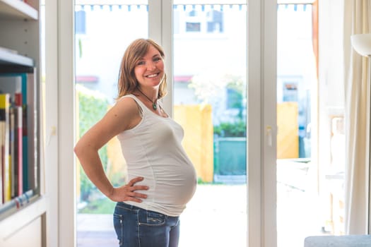 Happy Caucasian pregnant mother touching her tummy, blue jeans, close up