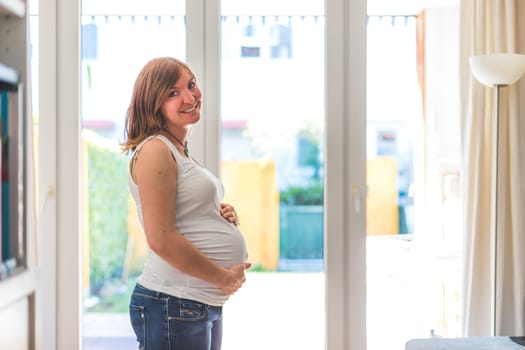 Happy Caucasian pregnant mother touching her tummy, blue jeans, close up