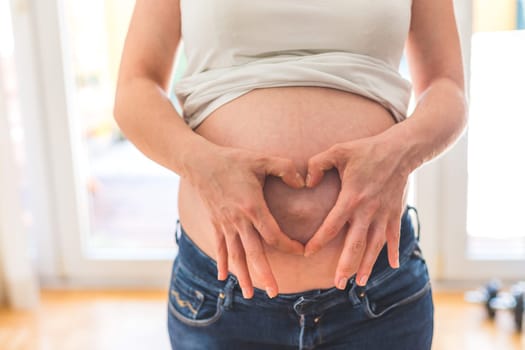 Happy Caucasian pregnant mother touching her naked tummy, blue jeans, close up