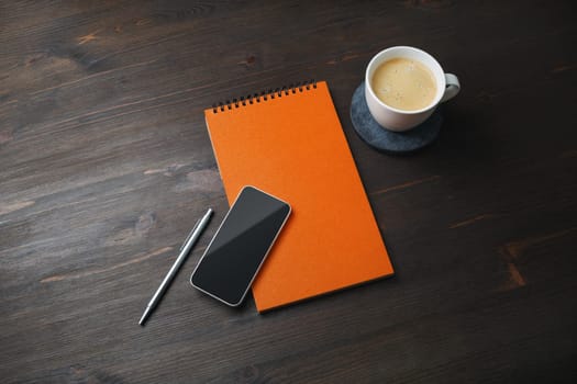 Smartphone, blank notepad, coffee cup and pen on wooden background. Template for placing your design.