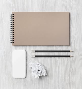 Blank corporate identity template on light wood table background. Notebook, smartphone, pencils and crumpled paper. Flat lay.