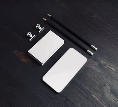 Smartphone, business cards and pencils on wood table background. Blank stationery set.