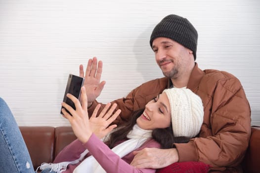 Happy couple greeting in a phone video call while relaxing on sofa in living room at home