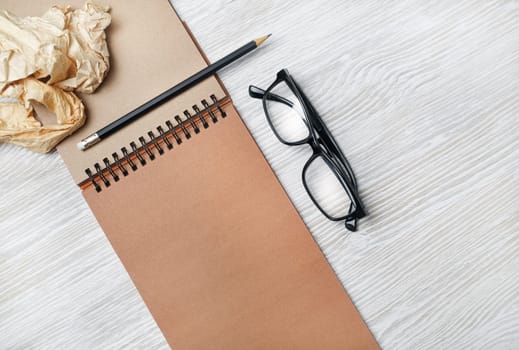 Photo of vintage notepad, glasses, pencil and crumpled paper on light wood table background. Responsive design template. Flat lay.