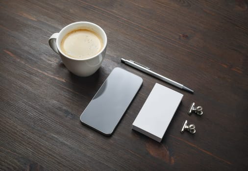 Smartphone, coffee cup, blank business card and pen on wooden background. Blank branding template.