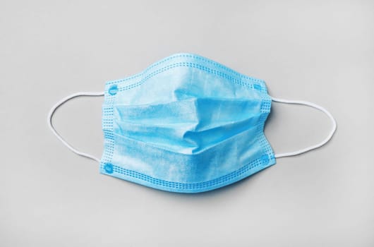 Blue medical face mask on paper background. Flat lay.