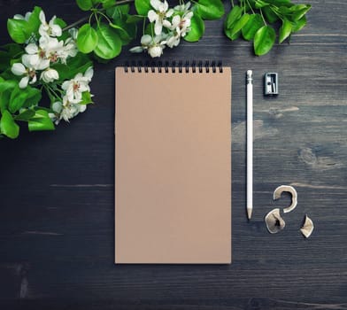 Blank kraft sketchbook, pencil, sharpener and flowers mock up on wooden background. Top view. Flat lay.