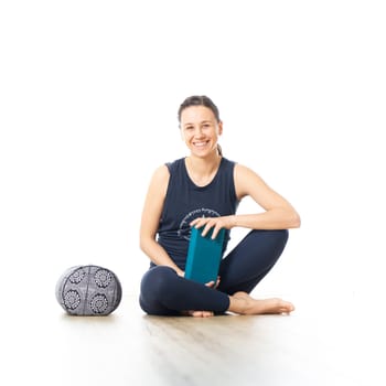 Restorative yoga with a bolster. Young sporty female yoga instructor in bright white yoga studio, smiling cheerfully while preparing restorative yoga exercise props.