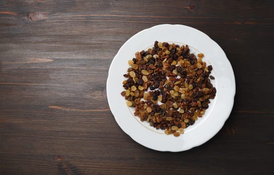 Raisins in plate on wood table background. Flat lay.
