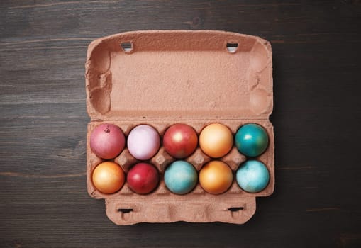 Packaging with colored Easter eggs on wood table background. Flat lay.