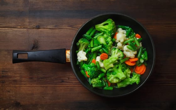 Fried vegetables in pan on wood table background. Flat lay.