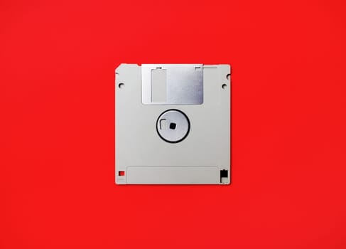 Gray diskette on red paper background. Floppy disc. Flat lay.