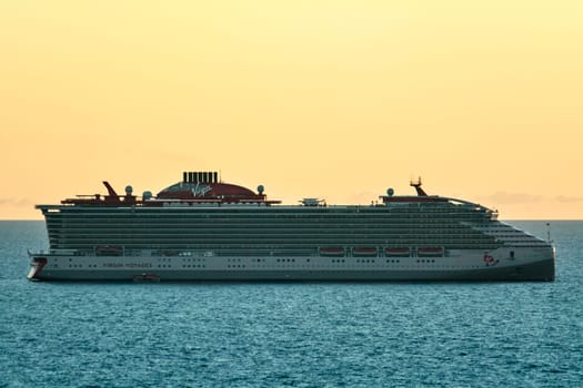 Civitavecchia. Italy - February 17, 2025: A large Virgin Voyages cruise ship sails on the calm sea during a beautiful sunset, showcasing its impressive size and modern design.