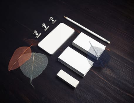 Brand ID template. Blank business cards, smartphone, pencil, eraser and leaves on wood table background.