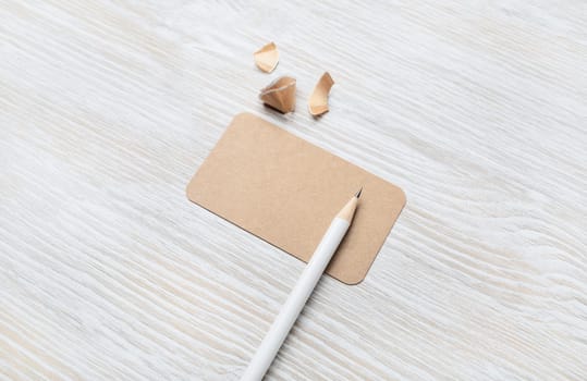 Blank kraft business card and pencil on light wood table background. Template for graphic designers portfolios.