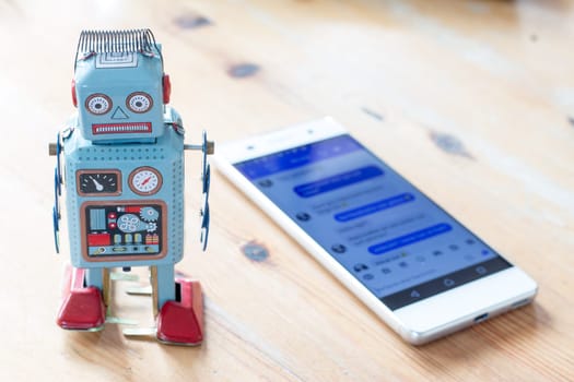 Toy robot and smartphone, symbol for chatbot and messenger