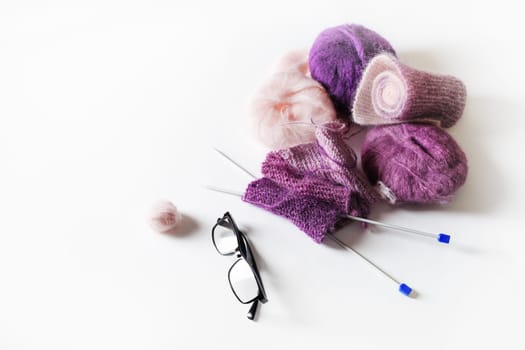 Knitting threads, knitting needles and glasses on white table background.