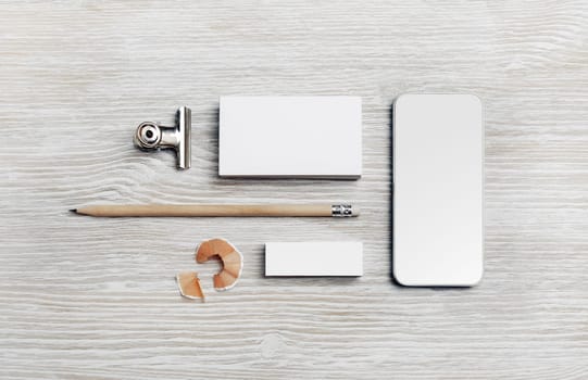 Branding mock up. Blank business card, smartphone, pencil and eraser on light wooden background. Flat lay.