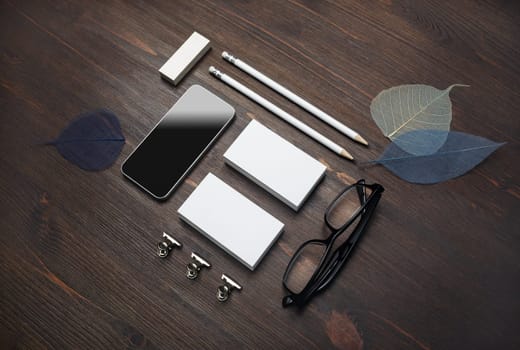 Branding stationery template. Blank business cards, smartphone, pencils, eraser, glasses and leaves on wood table background. For design presentations and portfolios.
