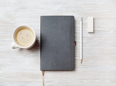 Blank notebook, pencil, eraser and coffee cup on light wooden background. Responsive design template. Top view. Flat lay.