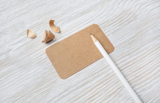 Blank kraft business card and pencil on light wooden background. Mock-up for branding identity.