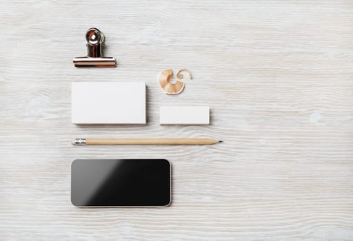 Smartphone and blank stationery: business card, pencil and eraser on light wooden background. Flat lay.